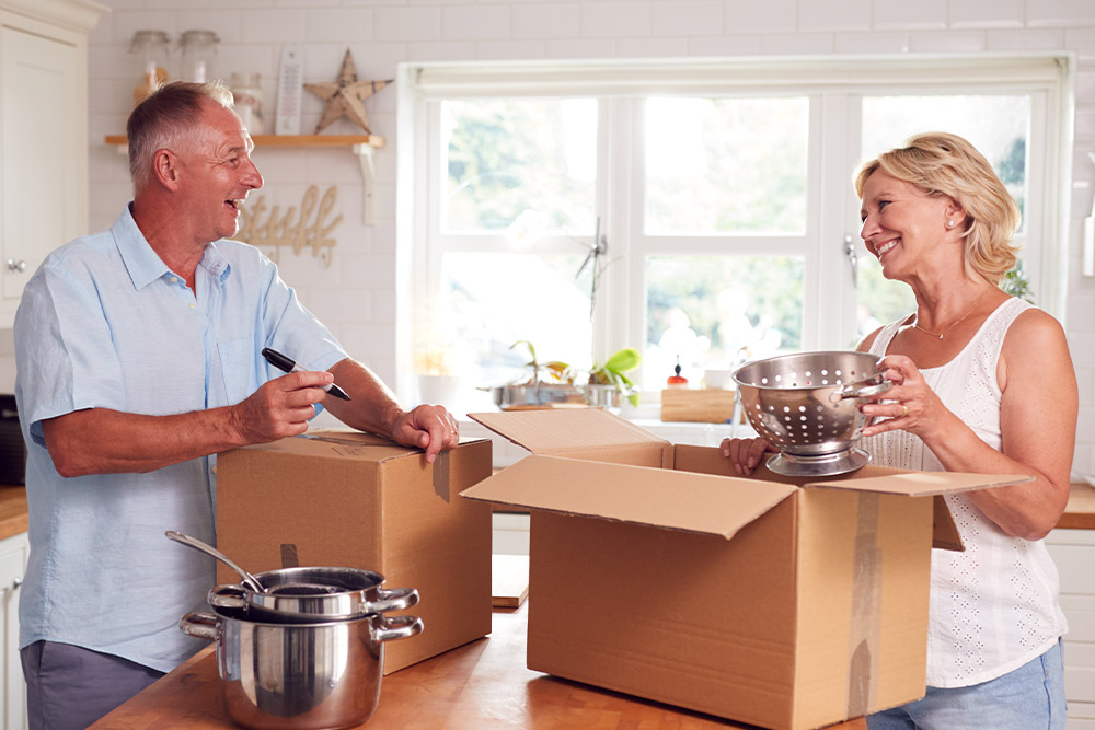 A Senior Couple Pack Dishes for Moving and Labels the Boxes Using a Marker